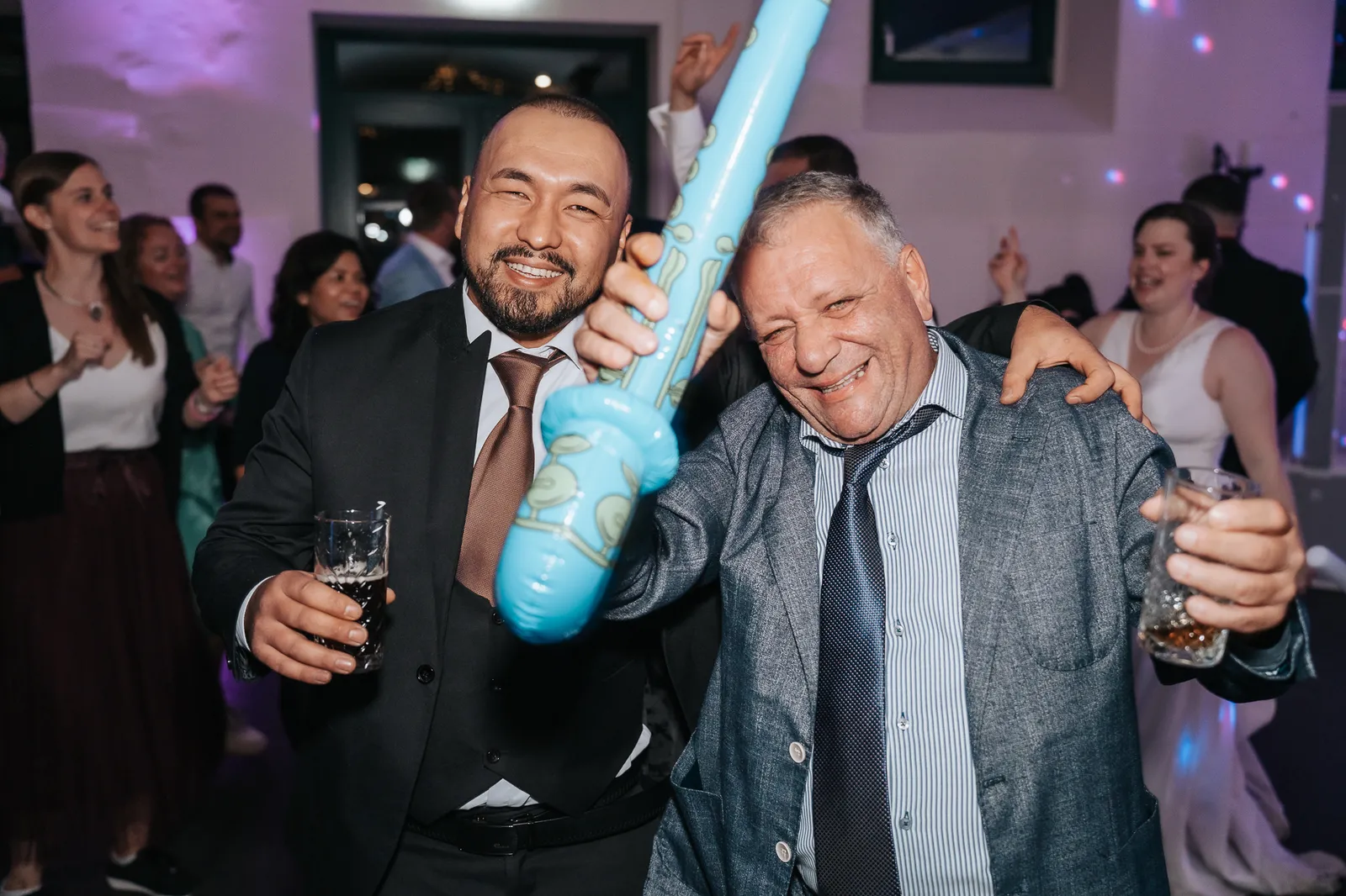 Zwei Gäste feiern ausgelassen auf der Tanzfläche und stoßen mit einem Glas an – Momentaufnahme der Hochzeitsfeier von Hélène & Massimo am Linslerhof, fotografiert by SB Snaps, Hochzeitsfotograf im Saarland.